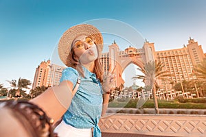 Asian girl traveller taking selfie photo with the famous luxury Atlantis hotel building on a Jumeirah Palm Island in Duba,