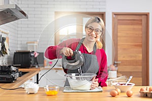 Asian girl using the blender, blend dough and other ingredients for cooking the chocolate cake with happy feeling in the kitchen