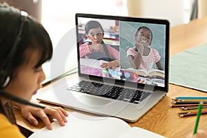 Asian girl using laptop for video call, with smiling diverse elementary school pupils on screen