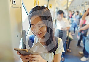 Asian girl using a smartphone in mass rapid transit among people