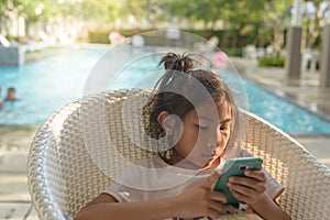 Asian girl using smartphone with swiming pool