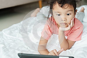 Asian girl are watching video that are exciting on online media. The little girl use the tablet to watch video for home