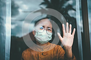 Asian girl wearing glasses, wearing a mask, looking out the window, is bored of having to detain and treat the illness at home photo