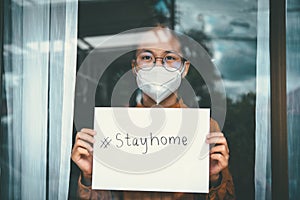 Asian girl wearing glasses, wearing a mask, holding paper labeled  stayhome, is bored of having to detain and treat the illness at