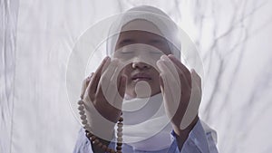 An Asian girl wearing a hijab is praying while holding prayer beads