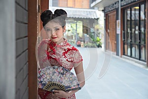 Asian girl wearing a red cheongsam holds a wooden fan in her hand. Posing for pictures