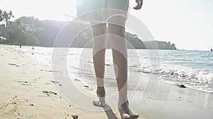 Asian girl wearing straw hat in casual dress with barefoot walking on the beach under sunlight. Low angle view.