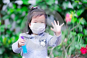 Asian girl wearing white face mask  in her hand holding a bottle of blue alcohol and lifting her hand  forbidding other people to
