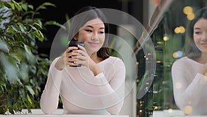 Asian girl woman smiling enjoying drinking fragrant delicious coffee hot tea morning cappuccino in cafe sitting at table