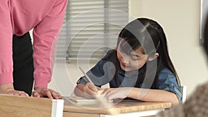 Asian girl writing or taking a note while teacher checking classwork. Pedagogy.
