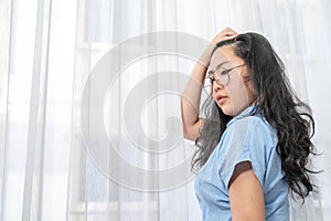 An Asian glasses woman in blue shirt  poses by slicks her hair back in front of lightening curtain photo