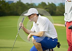 Asian golfer crouching in golf course aiming and preparing for putting