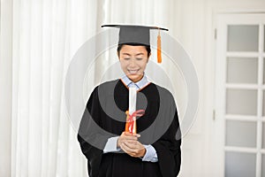Asian graduate in cap and gown smile and looking certificate or diploma proud of yourself,Graduated young woman holding diploma
