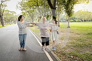 Asian granddaughter,daughter assisting senior mother to walking follow white line on the floor with the support at park, female
