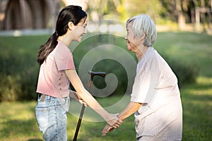 Asian granddaughter is giving a walking stick to her old grandmother,persuade her senior woman to take a walk,exercise in the