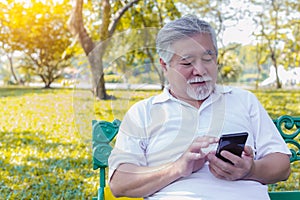 Asian grandfather chatting with family by using smart phone and internet online at park. Old man family stay at foreign country. E