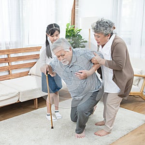 Asian grandfather fall down grandmother and granddaughter help and support carry him to sit on sofa,retirement life concept