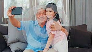 Asian grandfather and granddaughter video call at home. Senior Chinese grandpa happy with young girl using mobile phone video call