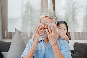 Asian grandfather relax at home. Senior Chinese, grandpa happy relax with young granddaughter girl enjoy close his eyes surprise