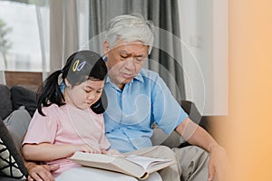 Asian grandfather relax at home. Senior Chinese, grandpa happy relax with young granddaughter girl enjoy read books and do