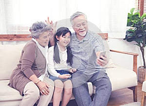 Asian Grandfather taking selfie with couple Grandparent and granddaughter with happy feeling by mobile phone in house, Long live
