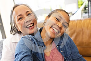Asian grandmother and biracial teenage granddaughter are smiling together at home
