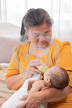 Asian grandmother feeding newborn baby in bedroom. Senior women taking care adorable infant at home. mother enjoying feeding