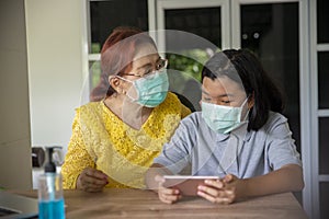Asian grandmother and Kid wear mask and  using mobile phone together. Thai Elderly Woman and Child greeting and hug at home. Happy