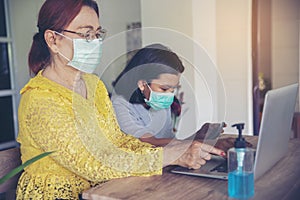 Asian grandmother and Kid wear mask and using mobile phone together. Thai Elderly Woman and Child sitting and learn online study