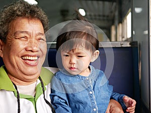 Asian grandmother laughing and smiling while enjoying holding her granddaughter as they traveling on a train together