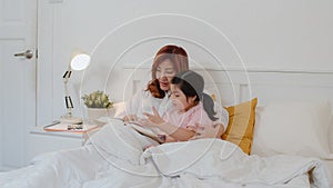 Asian grandmother read fairy tales to granddaughter at home. Senior Chinese, grandma happy relax with young girl enjoy good