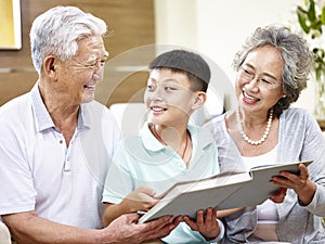 Asian grandparents and grandchild reading a book together