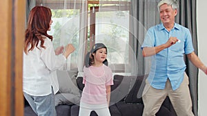 Asian grandparents and granddaughter listen to music and dance together at home. Senior Chinese, grandpa and grandma happy spend