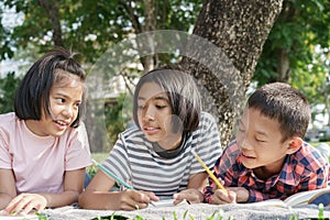 Asian Group elementary school children write a notebook with a pencil and learning together in the summer at park in the morning.