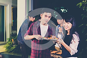 Asian group of friends having outdoor garden barbecue laughing with alcoholic beer drinks on night