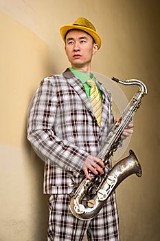 Asian guy with saxophone standing against a wall