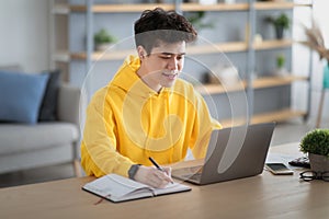 Asian guy sitting at desk, using pc writing in notebook