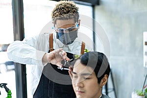 Asian hairdresser barber wear mask, cut hair of attractive man in shop. Handsome young man customer in modern salon barbershop,