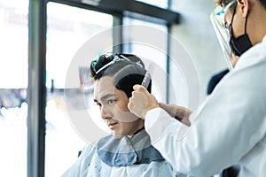 Asian hairdresser barber wear mask, cut hair of attractive man in shop. Handsome young man customer in modern salon barbershop,