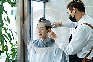 Asian hairdresser barber wear mask, cut hair of attractive man in shop. Handsome young man customer in modern salon barbershop,