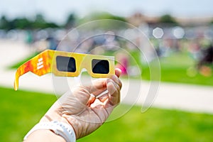 Asian hand wear smart watch holding paper solar eclipse with blurry crowd people watching totality show in Dallas, Texas