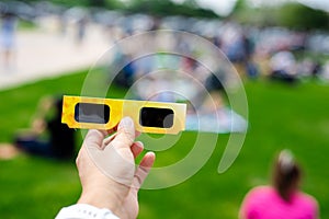 Asian hand wear smart watch holding paper solar eclipse with blurry crowd people watching totality show in Dallas, Texas