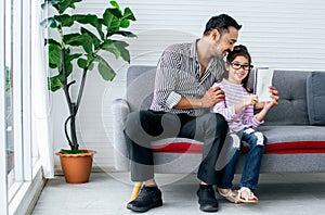 Asian handsome adult warm father and sweet cute little daughter girl sitting on sofa in living room at home, drawing, doing