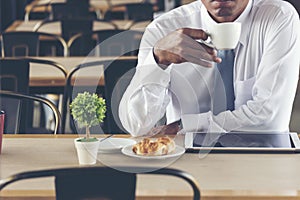 Asian Handsome businessman working outdoor in the coffee shop with laptop and holding cup of coffee on hand. Work outside office