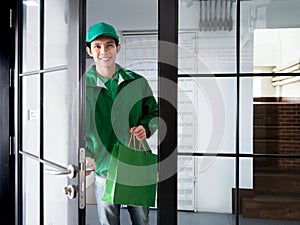 Asian handsome delivery man holding shopping paper bag and opening door to send food or product order by express service to