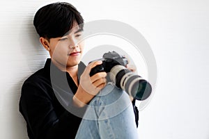 Asian handsome male model wearing casual black shirt with jeans, holding a camera, sitting on white background in a studio and