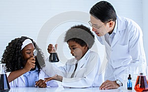 Asian handsome male teacher wearing eyeglasses and white gown uniform, teaching science and experiment to African black girl, boy