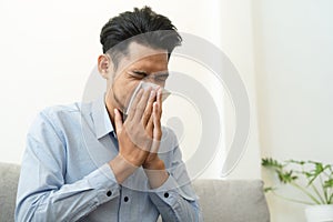 Asian handsome of  man having  flu season and sneeze using paper tissues sitting on sofa at home, Health and illness concepts