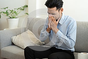 Asian handsome of man having flu season and sneeze using paper tissues sitting on a sofa at home, Health and illness concepts photo