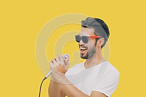 Asian handsome man with a mustache, smiling and singing to the microphone isolated on yellow background